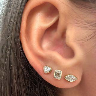 Close-up of an ear wearing three gold earrings with different designs.